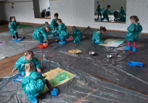 Dzieci w niebieskich strojach ochronnych malują na kartonach.
