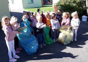 Dzieci prezentują zebrane śmieci posegregowane w workach według kolorów: niebieski, żółty, zielony, czarny.