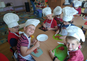 Dzieci w czapkach kucharza kroją pomiodory.
