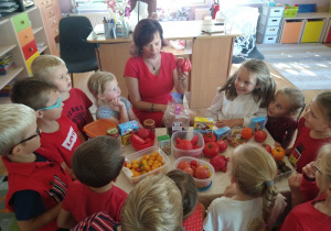 Dzieci w czerwonych strojach oglądają pomidory.