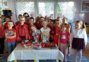 Dzieci stoją przed białym stolikiem, na którym leżą pomidory.