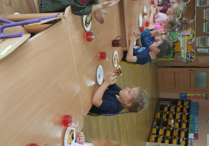 Grupa dzieci siedzących przy stole i konsumujących babeczki.